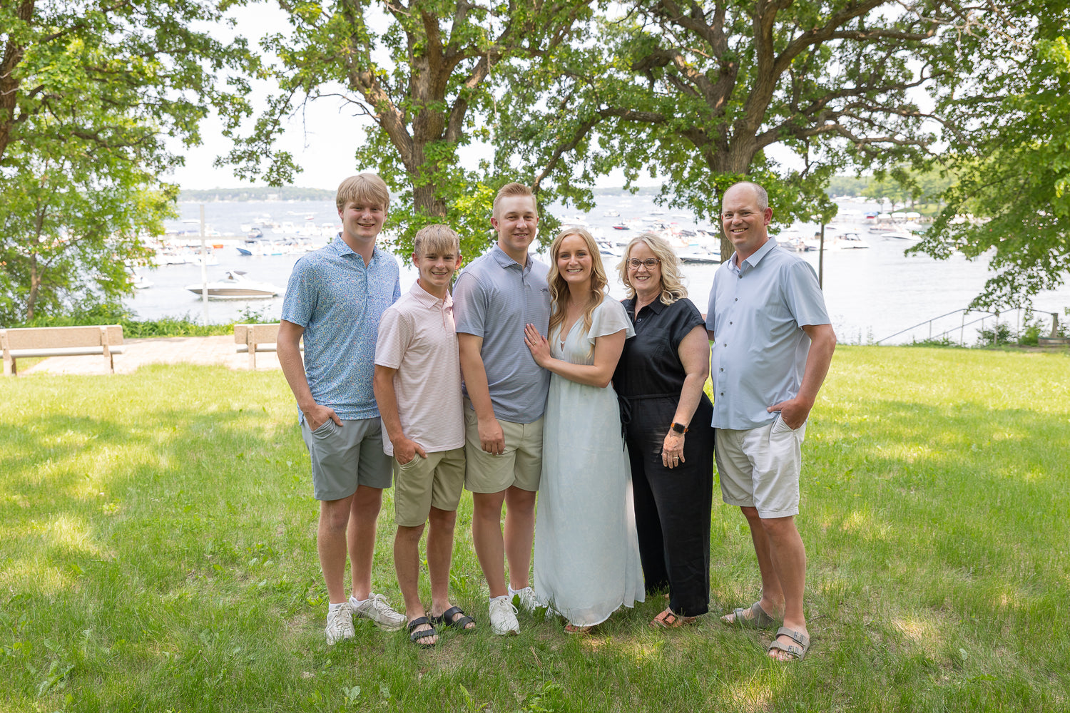 Family of six standing in a grassy area with trees and water in the background